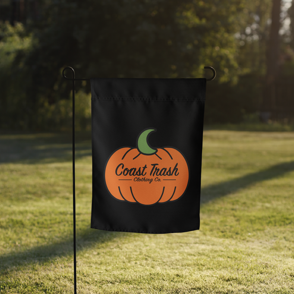 Coast Trash Halloween pumpkin garden flag displayed outdoors on a black flag stand